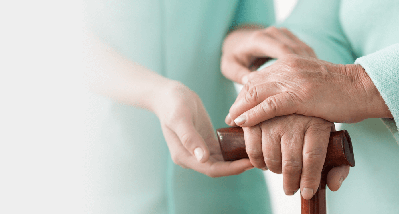 Closeup shot of a nurse's hand comforting an elderly patient’s hand on a cane.