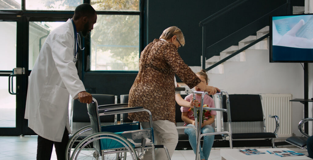 Doctor pushing a wheelchair as an older woman uses a walker during hospital discharge